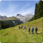 Wandergruppe vor Bergpanorama auf einer gründen Wiese.